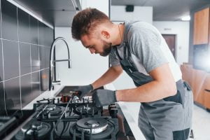 Young professional plumber in grey uniform working on the kitchen